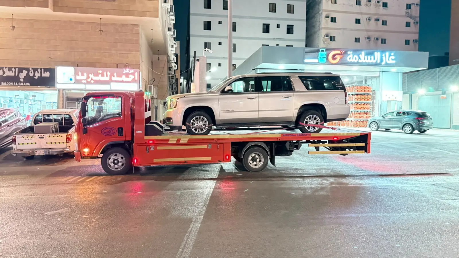 سطحة 24 ساعة تنقل سيارة جي إم سي يوكن ليلاً في شارع تجاري مضاء