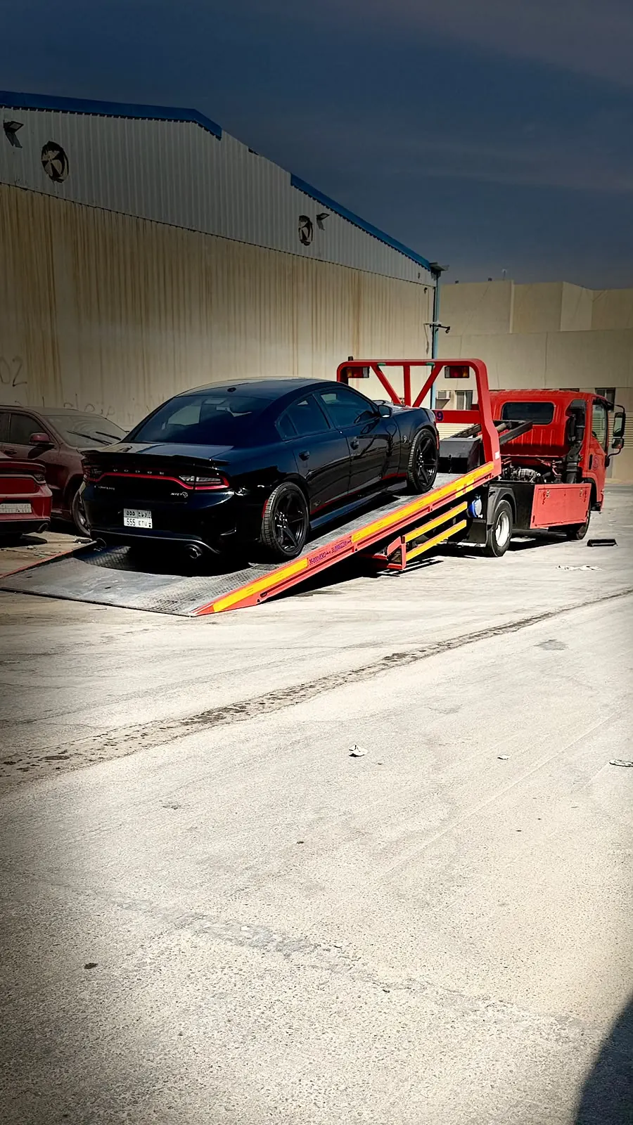 سطحة هيدروليك ترفع سيارة دودج تشارجر SRT سوداء في منطقة صناعية
